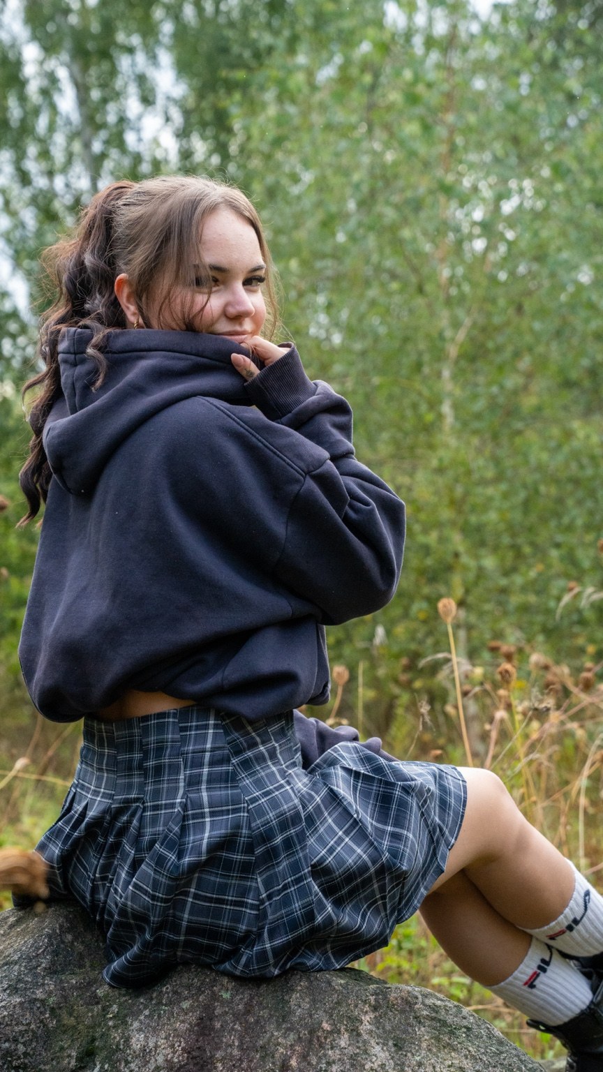 Frau im dunklen Hoodie auf einem Stein vor Bäumen