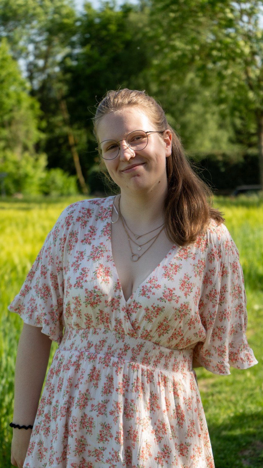 Porträt einer Frau mit Brille und Blumenkleid vor Bäumen